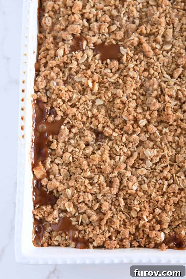 Gooey Caramel Apple Crumble 6 A close-up, top-down view of the bottom left corner of a white 9x13-inch pan filled with golden-brown caramel apple crisp, fresh from the oven.