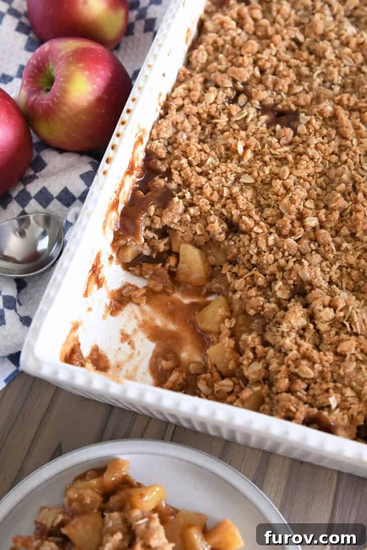 Gooey Caramel Apple Crumble 8 A top-down view of a freshly baked caramel apple crisp in a white 9x13-inch pan, with one inviting serving already removed from a corner.