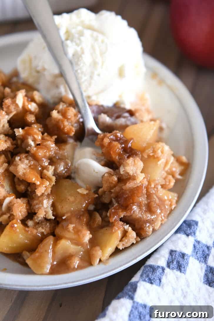 Gooey Caramel Apple Crumble 9 A delectable serving of caramel apple crisp on a gray plate, beautifully accompanied by a melting scoop of vanilla ice cream, promising a perfect taste experience.
