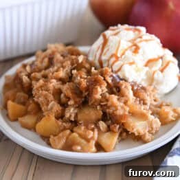 A comforting serving of caramel apple crisp on a gray plate, with a scoop of vanilla ice cream and an extra drizzle of caramel sauce.