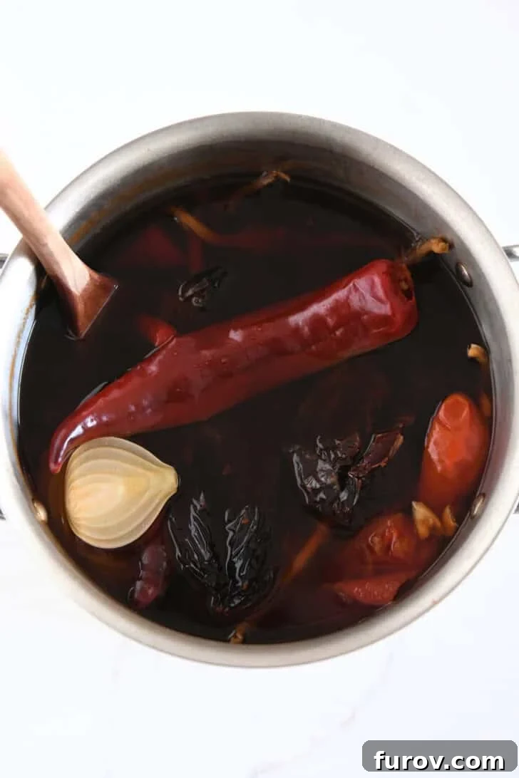 Ultimate Slow Cooker Birria Tacos 4 Top down view of pot with simmered broth of guajillo chiles, ancho chiles, arbol chiles, white onion, and garlic.