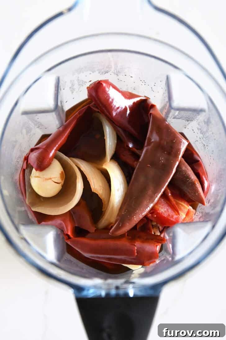 Ultimate Slow Cooker Birria Tacos 6 Top down view of blender with soft boiled Mexican chiles, cooked onions, and garlic.