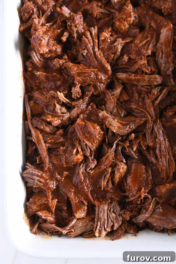 Ultimate Slow Cooker Birria Tacos 8 White 9X13-inch pan with shredded Mexican birria beef and broth.