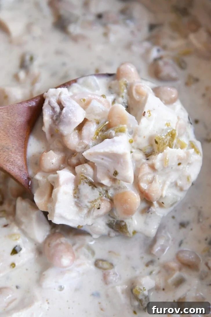 Velvety White Chicken Chili 5 Top down view of a wooden ladle full of creamy white chicken chili, showcasing its rich texture and delicious appeal.
