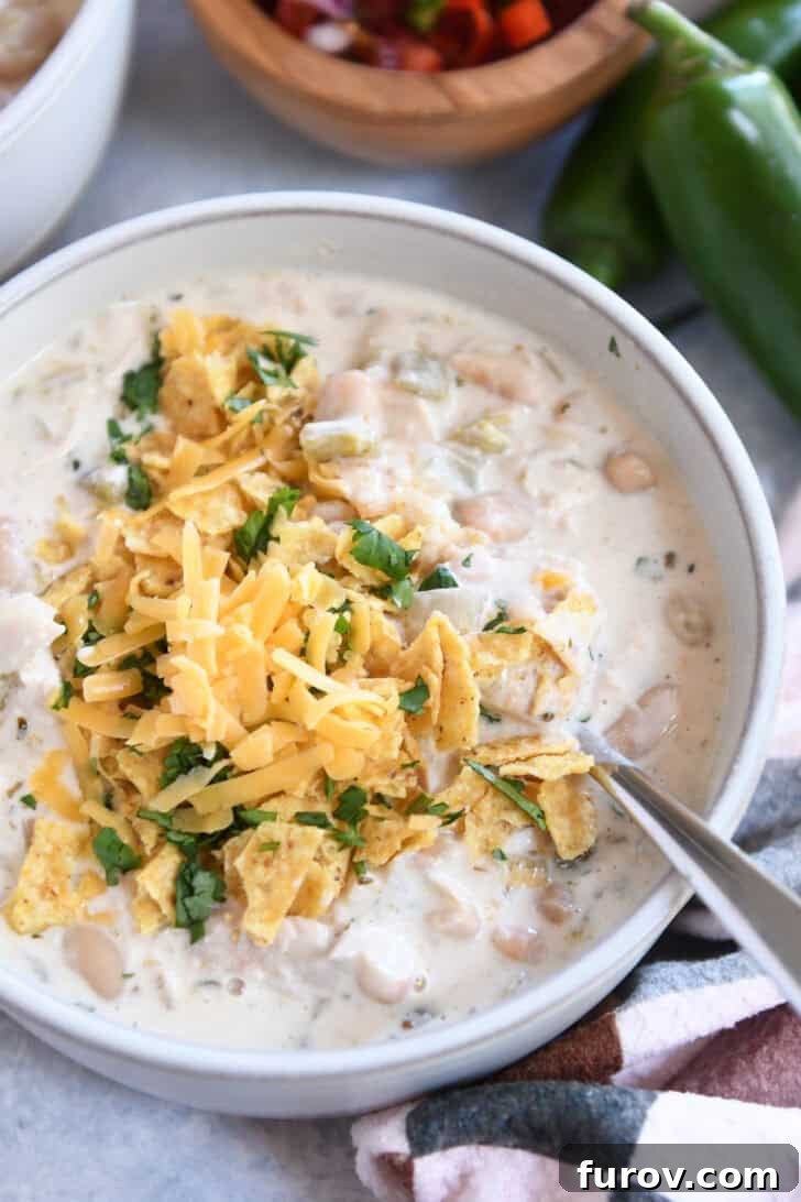Velvety White Chicken Chili 6 Top down view of a white bowl of white chicken chili topped with shredded cheddar cheese, chopped cilantro, and crushed tortilla chips, ready to be enjoyed.