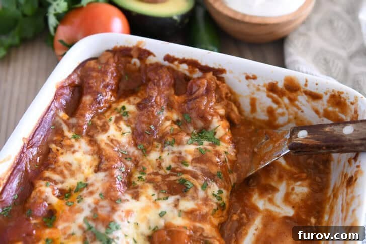 Square metal spatula scooping a portion of red sauce ground beef enchiladas from a white 9x13-inch pan, showcasing the delicious layers.