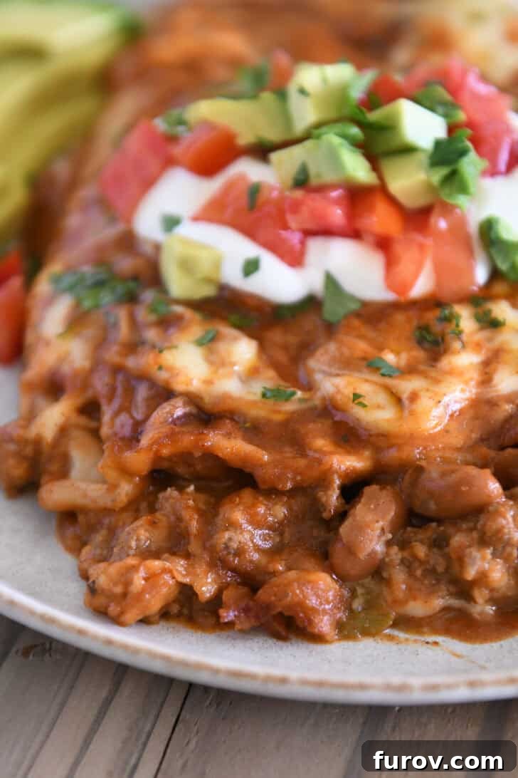 Close-up view of a single red sauce ground beef enchilada on a gray plate, revealing the savory ground beef and pinto bean filling.