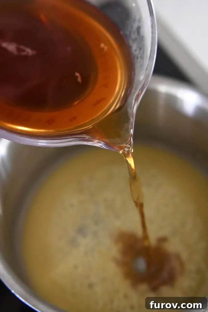 Pouring beef broth into a pan containing a roux made from olive oil and flour, as part of the enchilada sauce preparation.