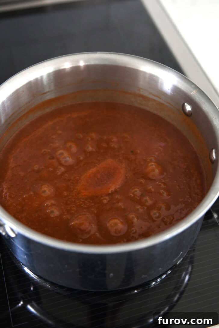 Homemade from-scratch red enchilada sauce simmering gently in a stainless steel saucepan on an induction stove, indicating perfect consistency.