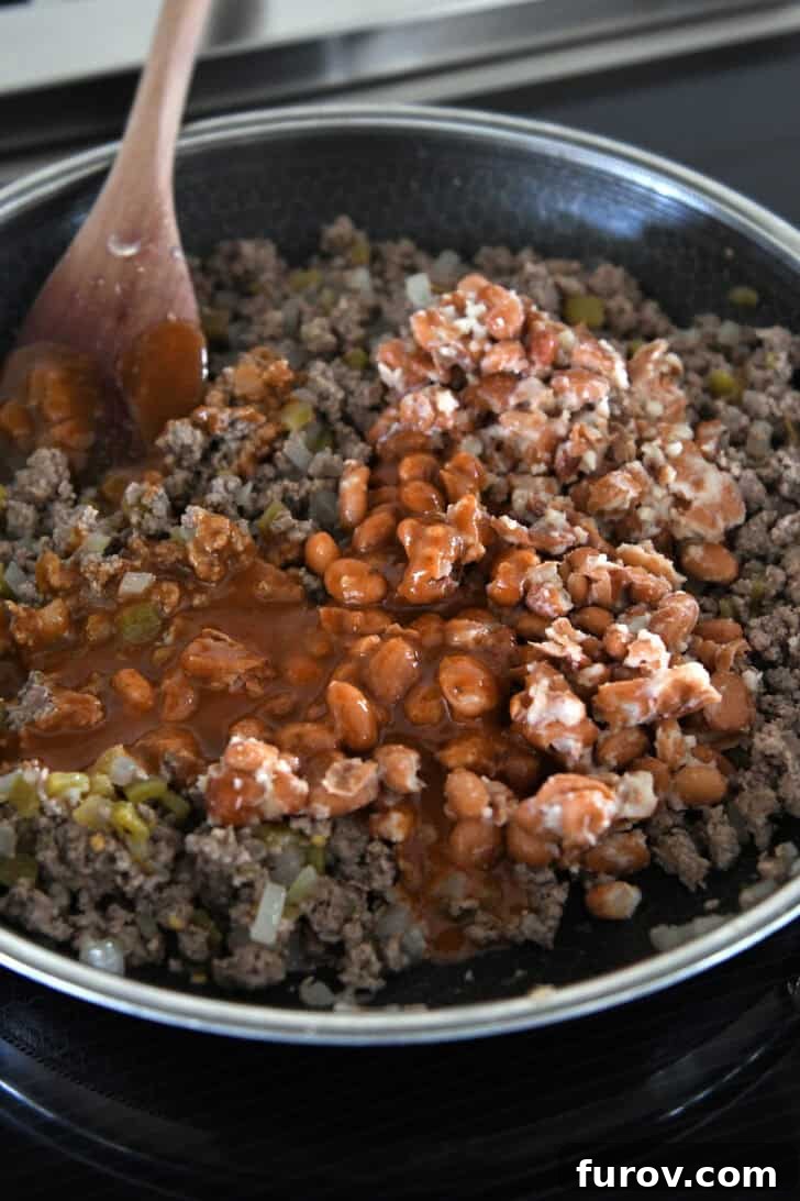 A 12-inch nonstick skillet displaying cooked ground beef, green chiles, and mashed pinto beans, all mixed with a portion of the red enchilada sauce.
