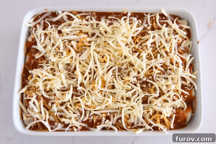 Top-down view of a white 9x13-inch baking pan, now completely filled with ground beef enchiladas, uniformly topped with the rich red enchilada sauce and a generous layer of shredded cheese, ready for baking.