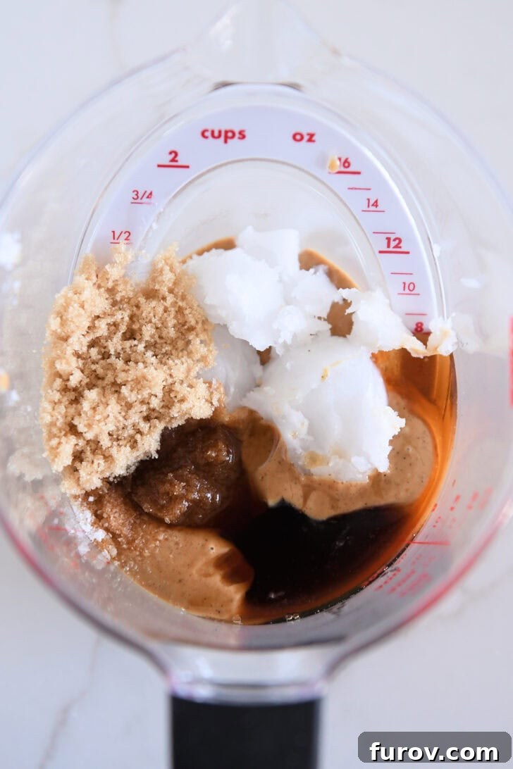 Liquid measuring cup filled with melted coconut oil, brown sugar, maple syrup, peanut butter, and vanilla extract, ready to be combined.