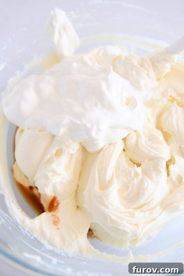 Golden Pumpkin Swirl Cheesecake 3 Glass bowl containing a creamy mixture of whipped cream cheese, sour cream, and vanilla extract, illustrating the smooth texture of the cheesecake base.
