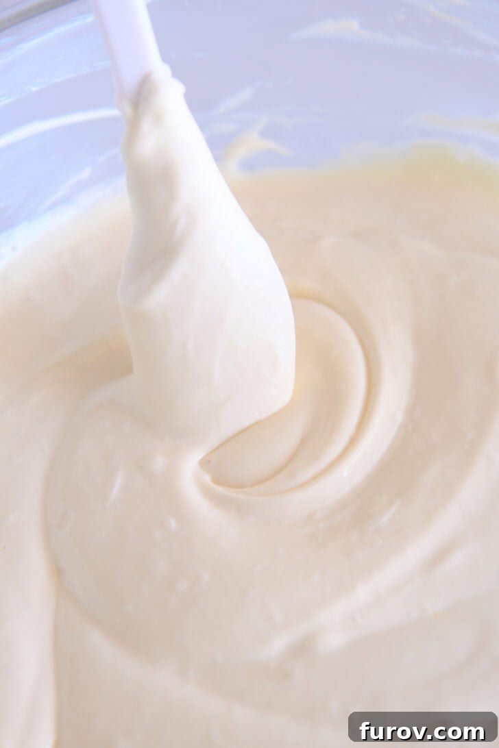 Golden Pumpkin Swirl Cheesecake 4 A white spatula gently stirring cheesecake batter in a glass bowl, showcasing the ideal consistency before dividing.