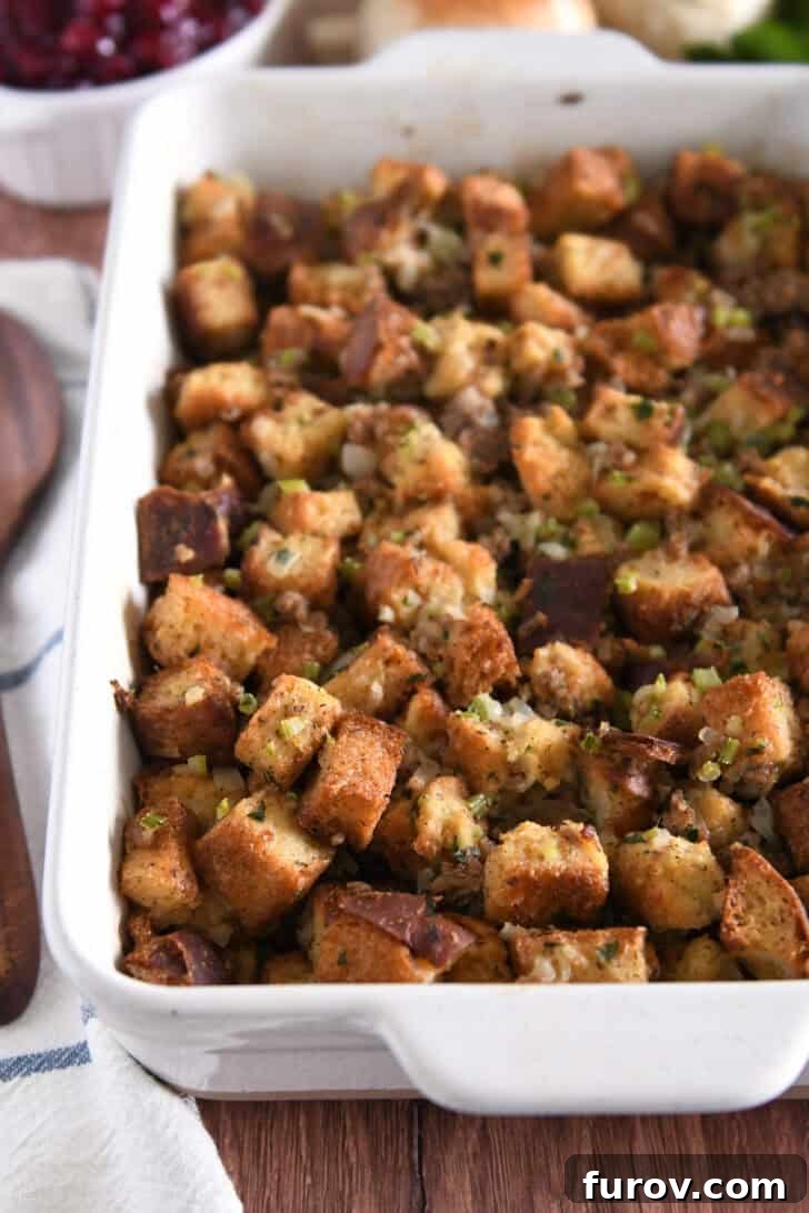 White 9X13-inch pan with baked sausage and herb stuffing, golden brown and garnished with fresh herbs.