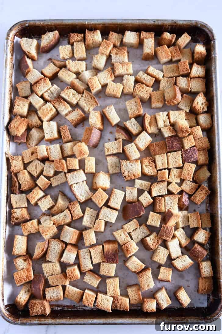 Sheet pan with evenly spread toasted bread cubes, golden and dry.