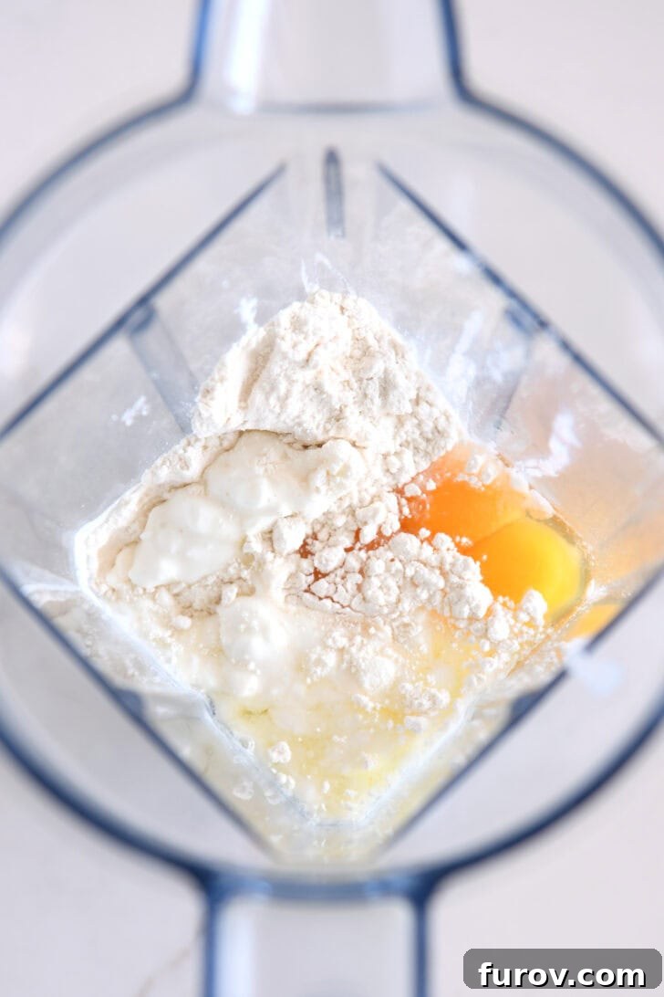 Top down view of blender with cottage cheese, flour, eggs, baking powder and salt before blending.