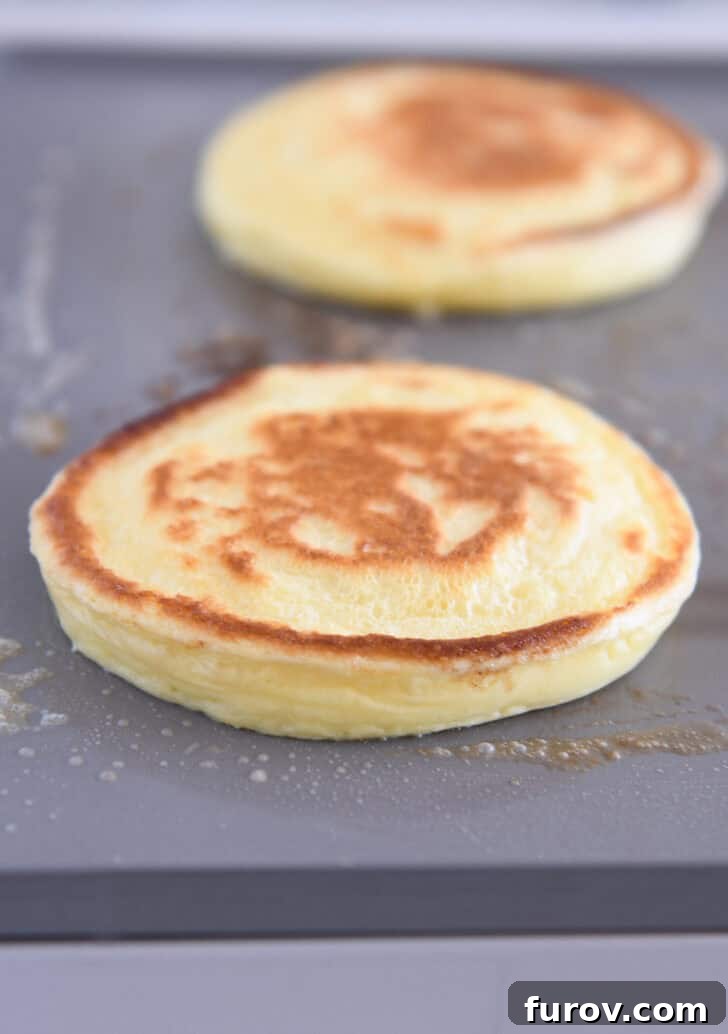 A fluffy cottage cheese pancake cooking on a buttered griddle, showing bubbles on the surface.