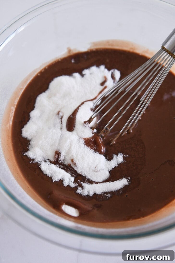 Velvet Chocolate Perfection 4 A glass bowl containing a glossy, liquid chocolate mixture, granulated sugar, and a wire whisk, illustrating the smooth preparation process for the pie filling.