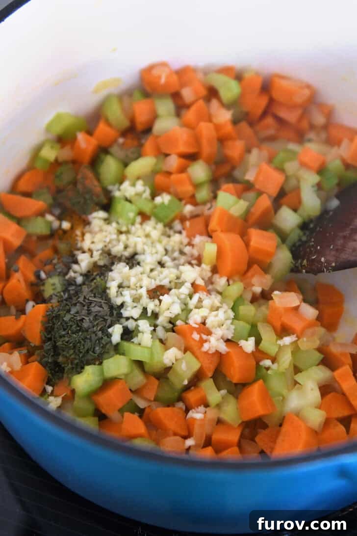 Cast iron pot showing diced celery, carrots, onions, dried basil, and minced garlic ready to be sautéed for soup base.