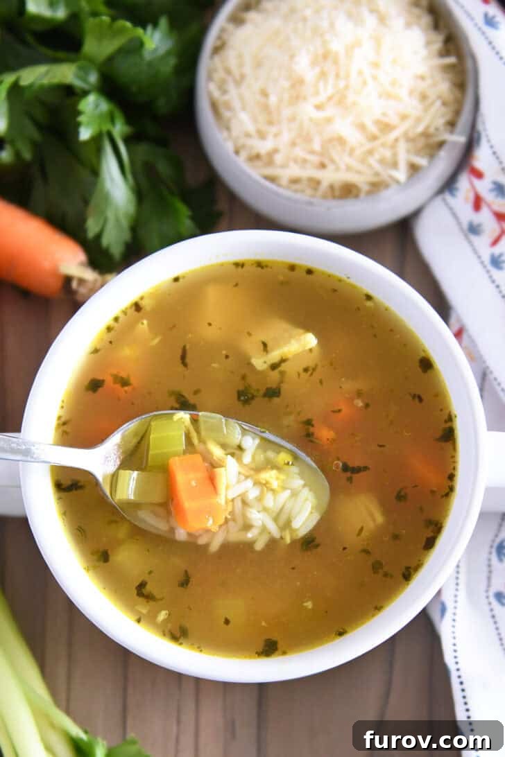 Spoon lifting a generous scoop of chicken and rice soup from a white bowl, garnished with fresh parsley and Parmesan cheese.