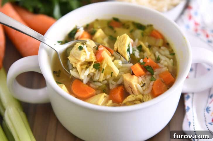 Spoon lifting a scoop of chicken and rice soup from a white bowl, generously topped with fresh parsley and grated Parmesan cheese.