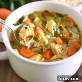 Spoon lifting up scoop of chicken and rice soup in white bowl with handles topped with fresh parsley and Parmesan cheese.