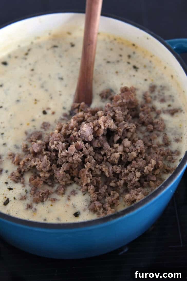 Cooked, crumbled sausage in soup pot with creamy soup.