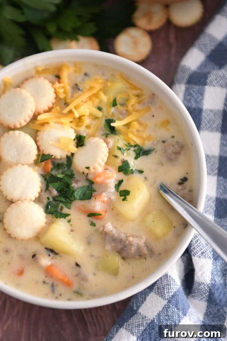 Soup bowl with sausage potato soup topped with oyster saltine crackers, fresh parsley and grated cheese and spoon on side.