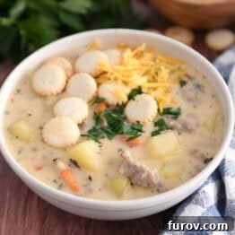Soup bowl with sausage potato soup topped with oyster saltine crackers, fresh parsley and grated cheese.