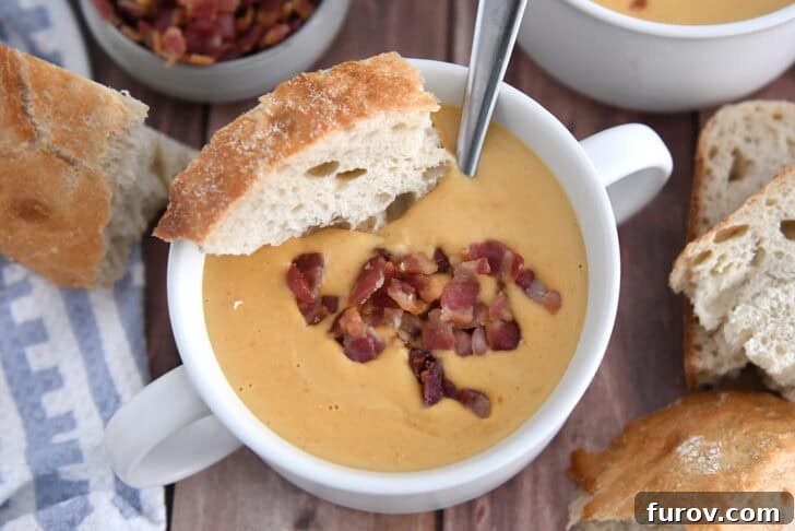 Top down view of creamy roasted butternut squash soup in a white bowl, garnished with crusty bread and crispy bacon pieces.