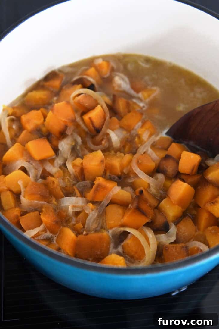 Soup pot with a wooden spoon stirring fragrant broth, roasted butternut squash pieces, and sweet onions.