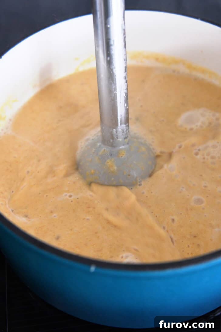 Immersion blender smoothly pureeing butternut squash soup directly in the soup pot, creating a creamy texture.