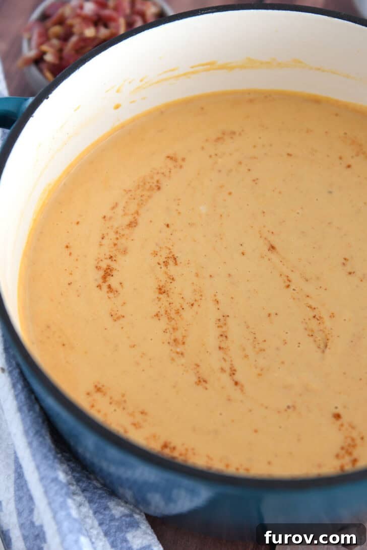 Smooth, blended butternut squash soup in a soup pot, with a sprinkle of red cayenne pepper on top.