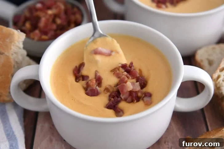 A spoon scooping a delicious bite of creamy butternut squash soup from a white bowl, topped with savory cooked bacon pieces.