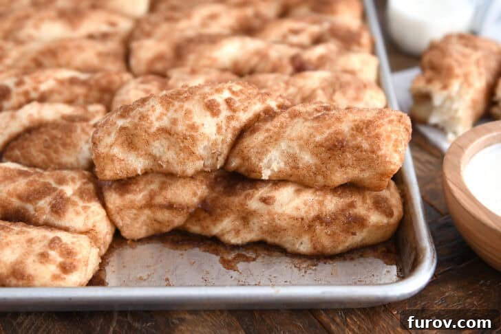 Baked pan of cinnamon sugar twists with one piece stacked on top of another, showing their beautiful golden-brown finish.