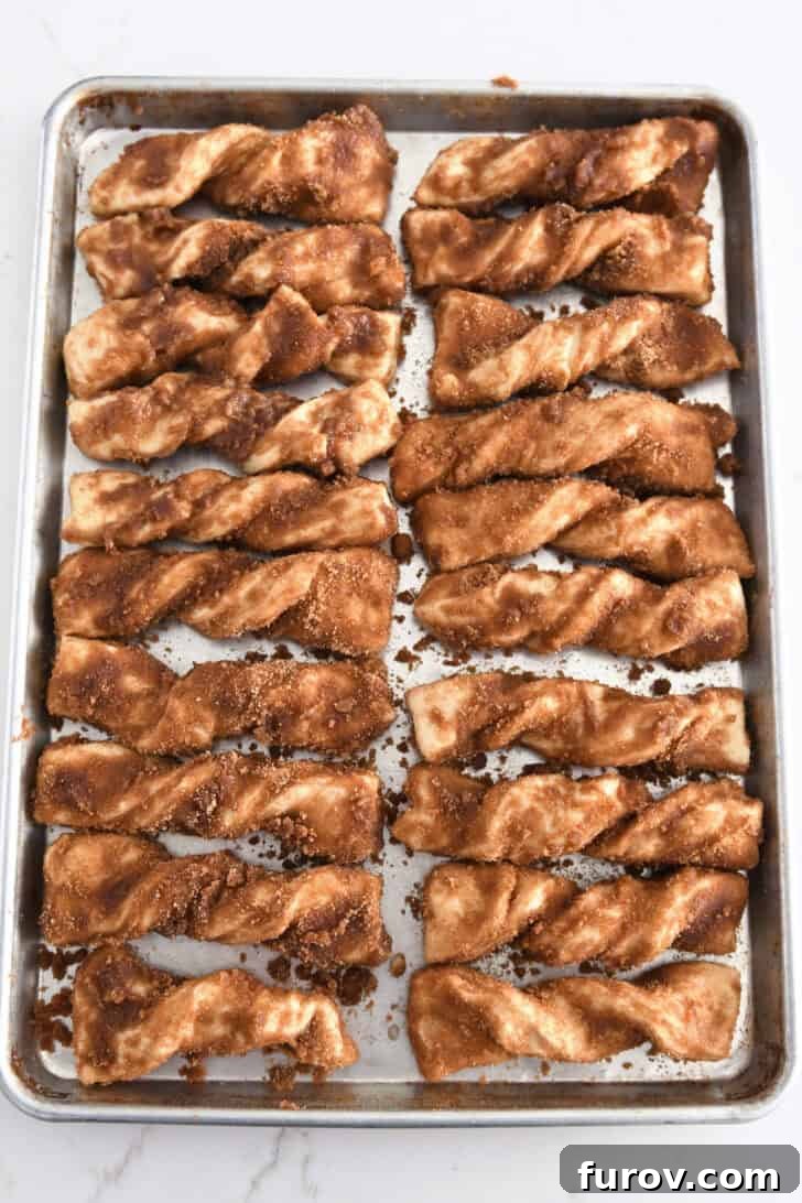 Twenty twisted cinnamon sugar dough strips neatly arranged on a half sheet pan, ready for their second rise and baking.