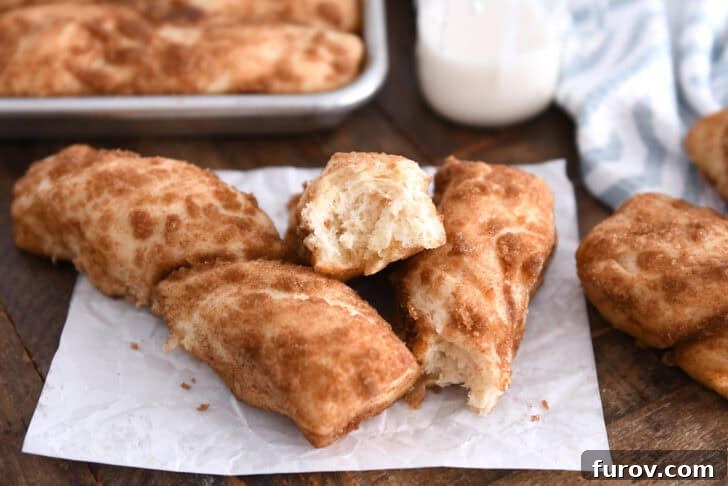 Three cinnamon sugar twists on white parchment paper, with one broken in half to reveal its fluffy interior.