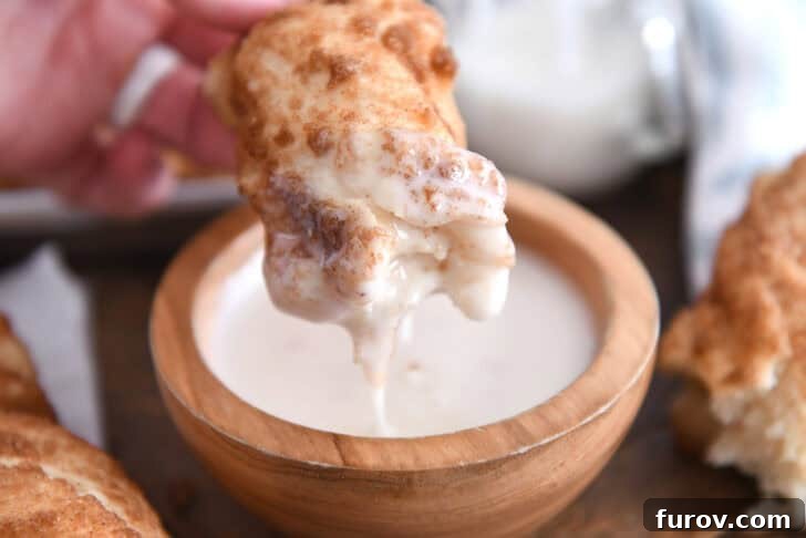A buttery cinnamon sugar twist being dipped into a small white bowl of sweet, creamy icing.