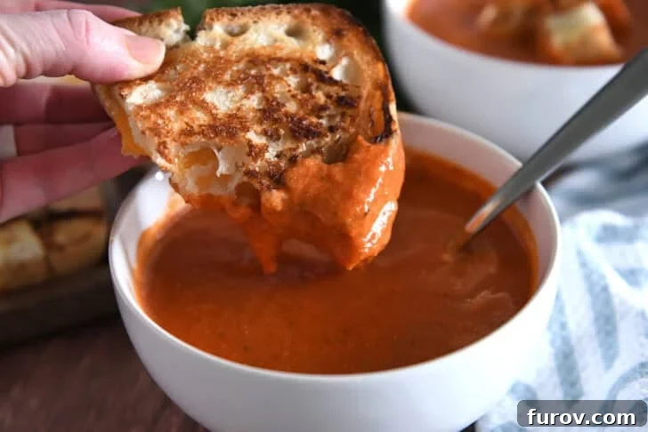 White bowl with homemade tomato soup and half a grilled cheese dipped in the soup.