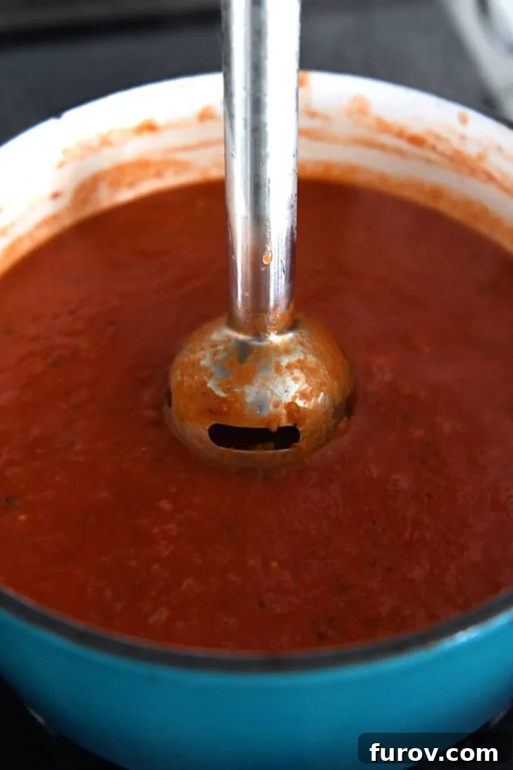 Immersion blender in cast iron enamel pot of tomato soup.