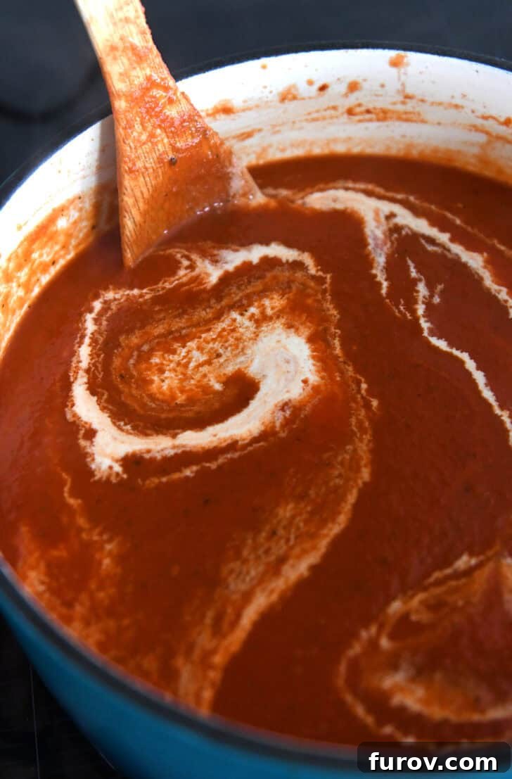 Cast iron enamel pot with homemade tomato soup and swirls of heavy cream.