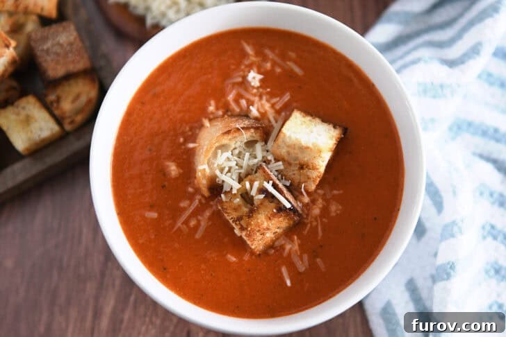 Top down view of white bowl filled with homemade tomato soup, homemade croutons and parmesan cheese.