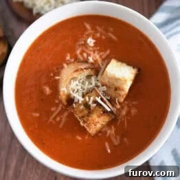 Top down view of white bowl filled with homemade tomato soup, homemade croutons and parmesan cheese.