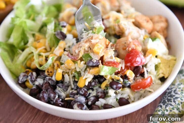 A white bowl with a fork scooping up a flavorful combination of cilantro lime rice, black beans, roasted corn, tender chicken, and a drizzle of creamy dressing, capturing the essence of a perfect bite.