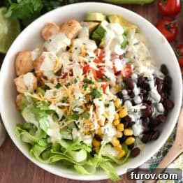 A visually appealing white bowl generously filled with cooked chicken, fresh chopped tomatoes, cilantro lime rice, creamy avocado chunks, black beans, roasted corn, and crisp lettuce, ready for a delicious meal.