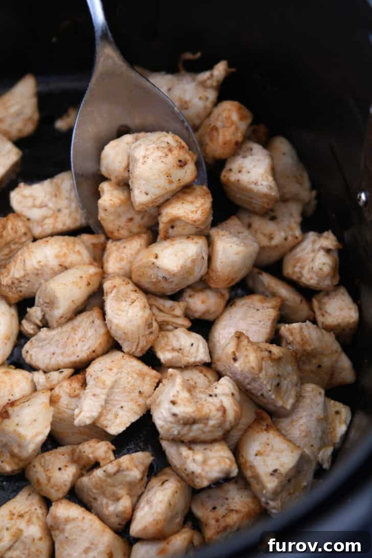 Perfectly cooked, diced chicken pieces, glistening with marinade, spread out in the basket of an air fryer.