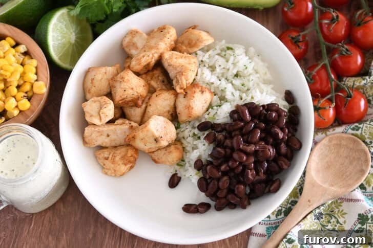 A white bowl showcasing cilantro lime rice, cooked chicken, and a generous serving of seasoned black beans.