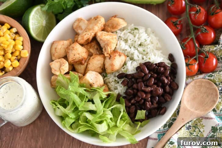 A white bowl filled with cilantro lime rice, flavorful chicken, black beans, and a bed of crisp shredded lettuce.