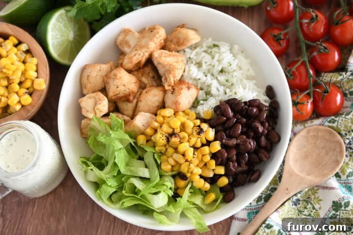 A white bowl featuring cilantro lime rice, chicken, black beans, refreshing lettuce, and vibrant roasted corn kernels.